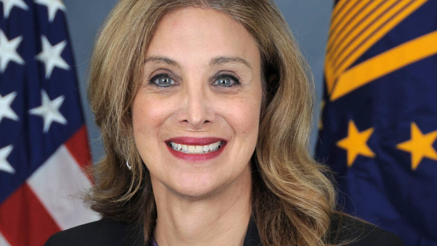 Amanda Simpson smiling in an official portrait with U.S. and navy flags behind.