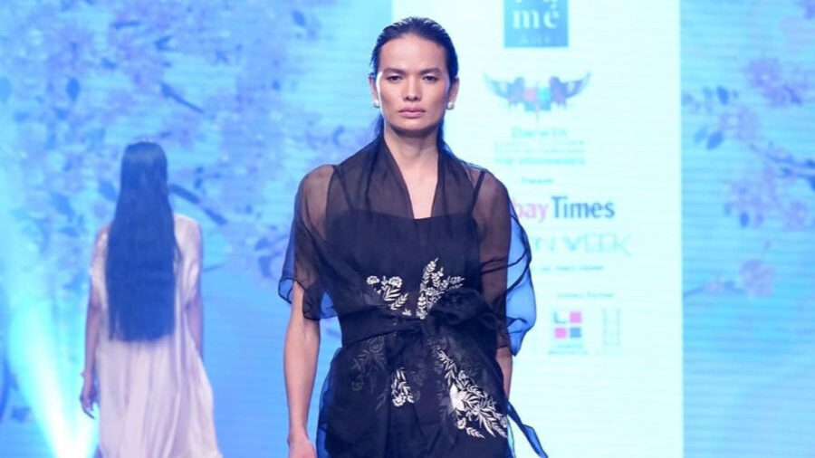 Anjali Lama walking a runway in a black outfit with floral design at Fashion Week India 2022.