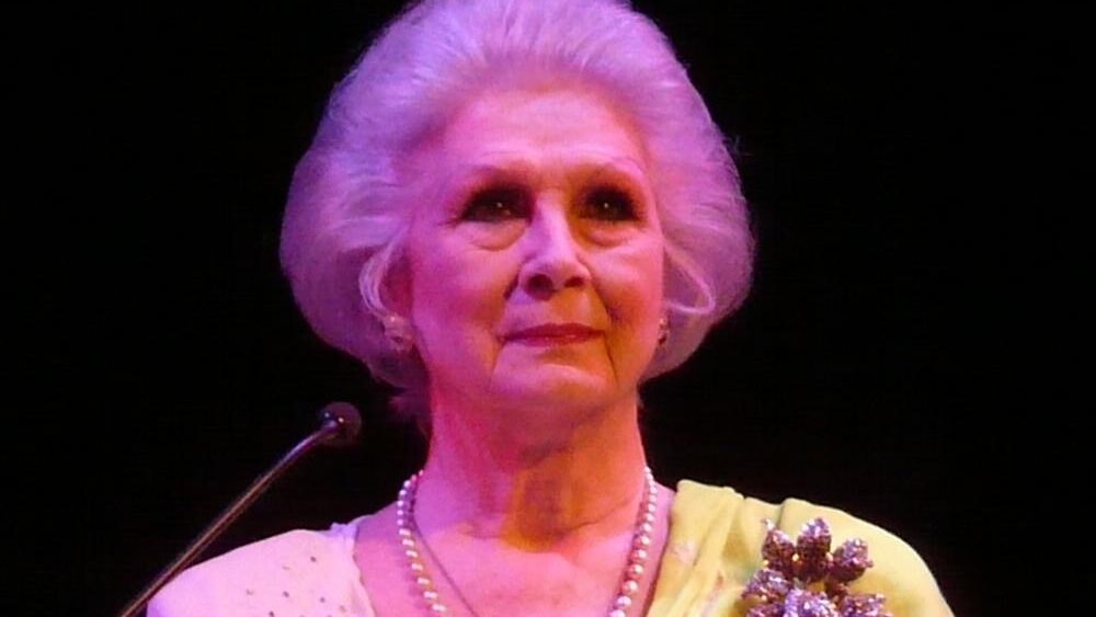 April Ashley standing on stage at the Southbank Centre, London, wearing a pearl necklace and a floral brooch, February 2009.
