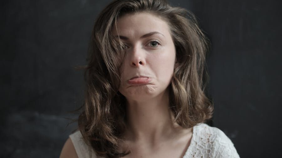 Woman with shoulder-length hair making an exaggerated pouty face, showing humorous disappointment in front of a dark background.