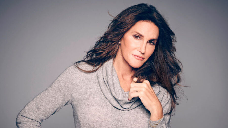 Caitlyn Jenner en una pose serena con la mano cerca del cuello, el cabello peinado y un fondo neutro.