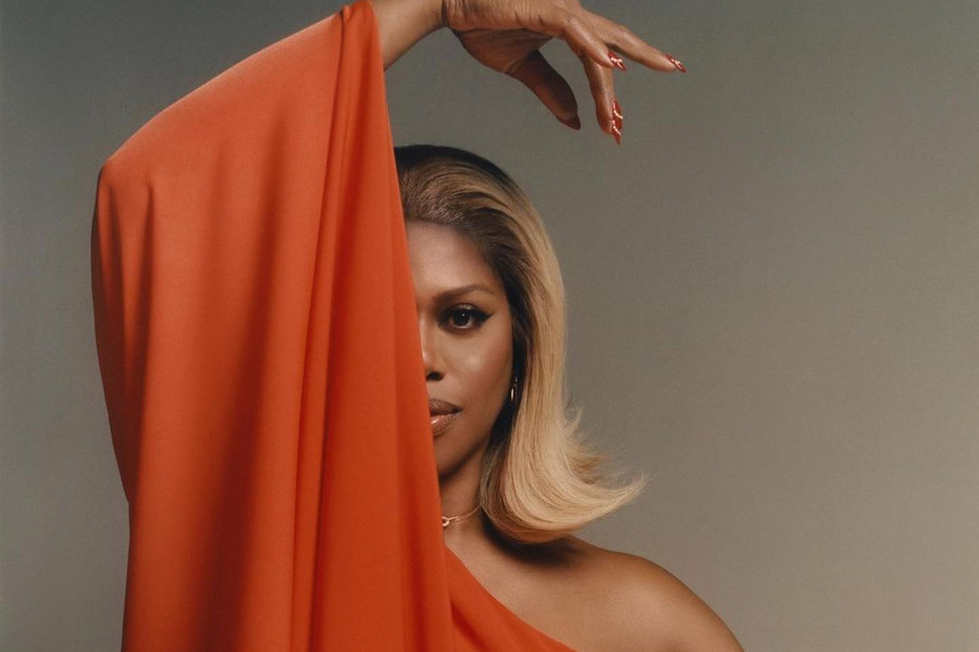 Laverne Cox poses in an orange one-sleeve dress, one eye covered by her arm, in a promotional portrait for Inventing Anna.
