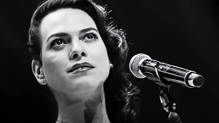 Black-and-white photo of Daniela Vega in front of a microphone on stage, looking up with soft lighting.