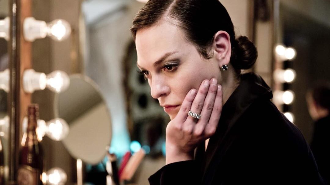 Daniela Vega in character as Marina, leaning on hand in front of mirror backstage, warm ambient lighting.