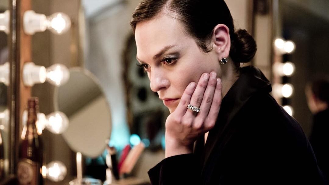 Daniela Vega en Marina, appuyée sur sa main devant un miroir en loge, lumière chaude d’ambiance.