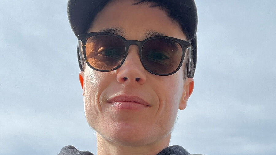 Selfie de Elliot Page al aire libre, con gorra, sudadera y arnés negro.