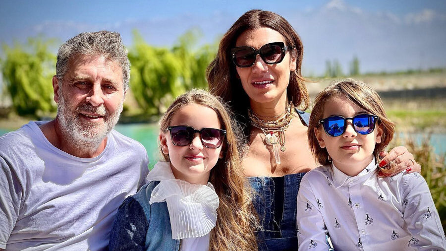 Florencia de la V smiles with her husband and twins at an outdoor lunch table, all wearing sunglasses.
