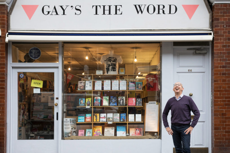 Exterior view of the LGBTQ+ bookstore Gay’s The Word, with a man standing in front and red triangle signs above.