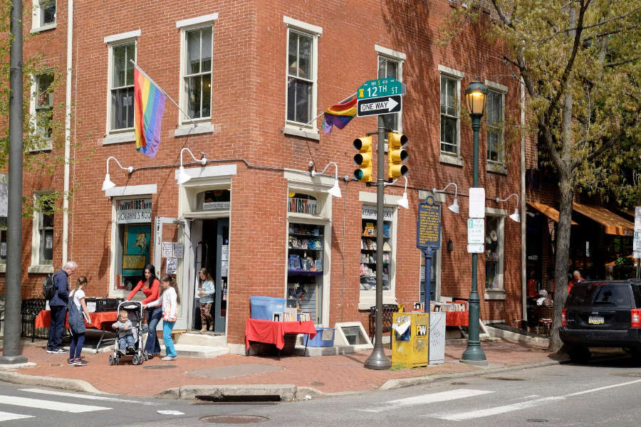 Exterior of Philly AIDS Thrift @ Giovanni’s Room with rainbow flags, books displayed outside, and people walking by.