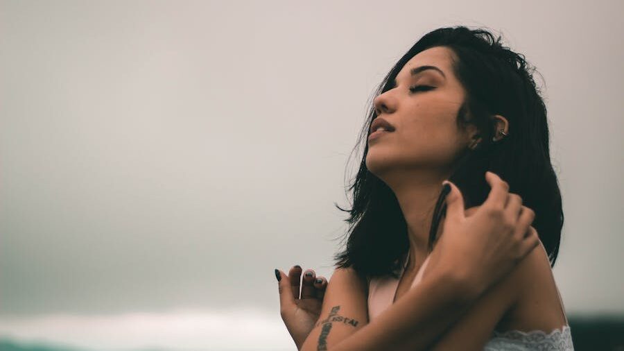 Woman with short dark hair closing her eyes and holding herself calmly under a grey sky.