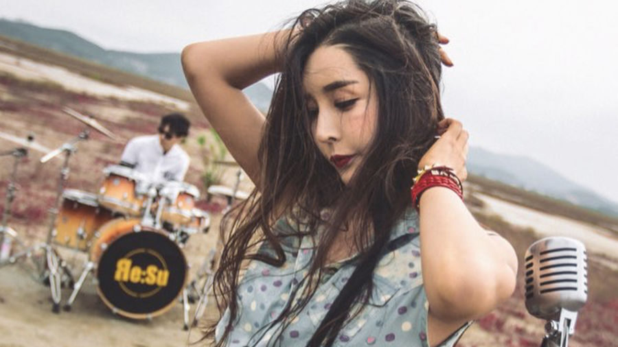 Harisu posa con un micrófono vintage en un campo, mientras un baterista toca detrás de ella una batería Re:Su.