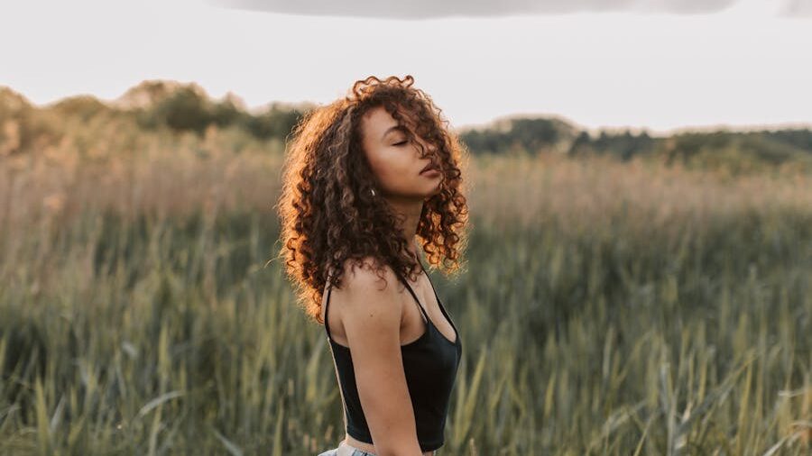 Portrait of a young woman with voluminous curls, wearing a black top, surrounded by nature.