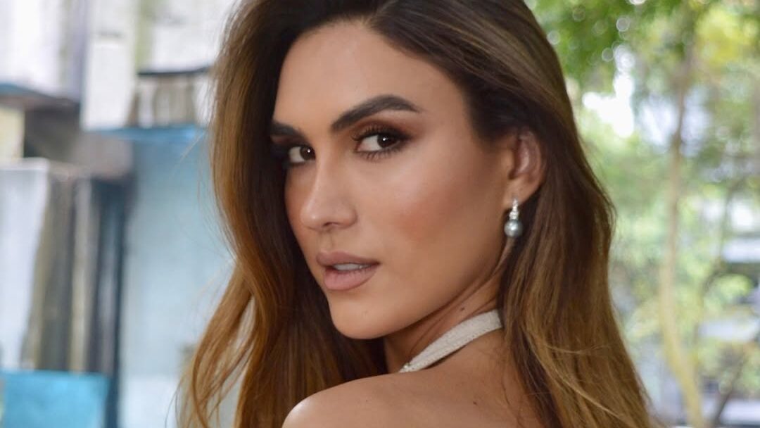 Isabella Santiago en robe blanche regarde l’objectif dans un parc.