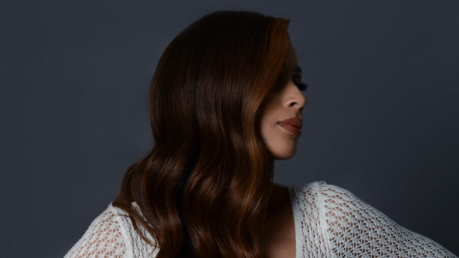 Isis King in a side pose wearing a white crochet dress with long sleeves and over 600 tassels, hair cascading in waves.