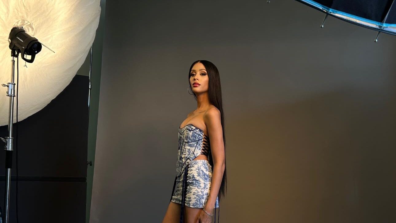 Isis King posing in a short strapless printed dress and red heels during a studio photoshoot, December 2023.