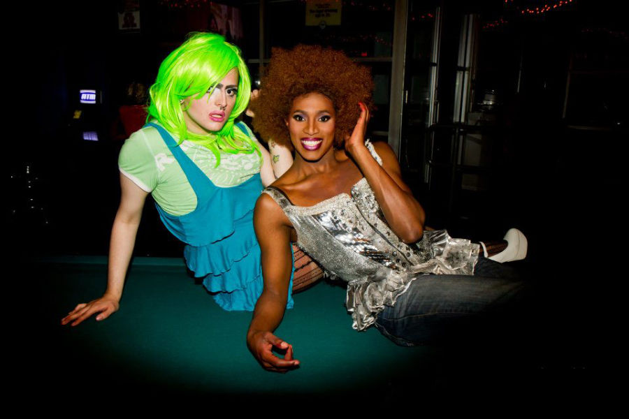 Two drag queens in bold wigs and dresses pose playfully on a pool table at Jacques.