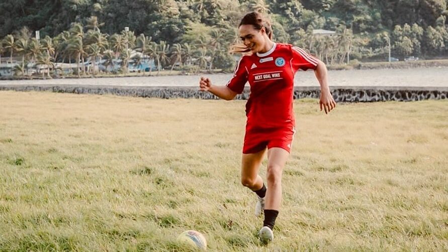 Jaiyah Saelua en tenue rouge frappant un ballon sur le terrain de Fagaalu Park, entourée de palmiers.