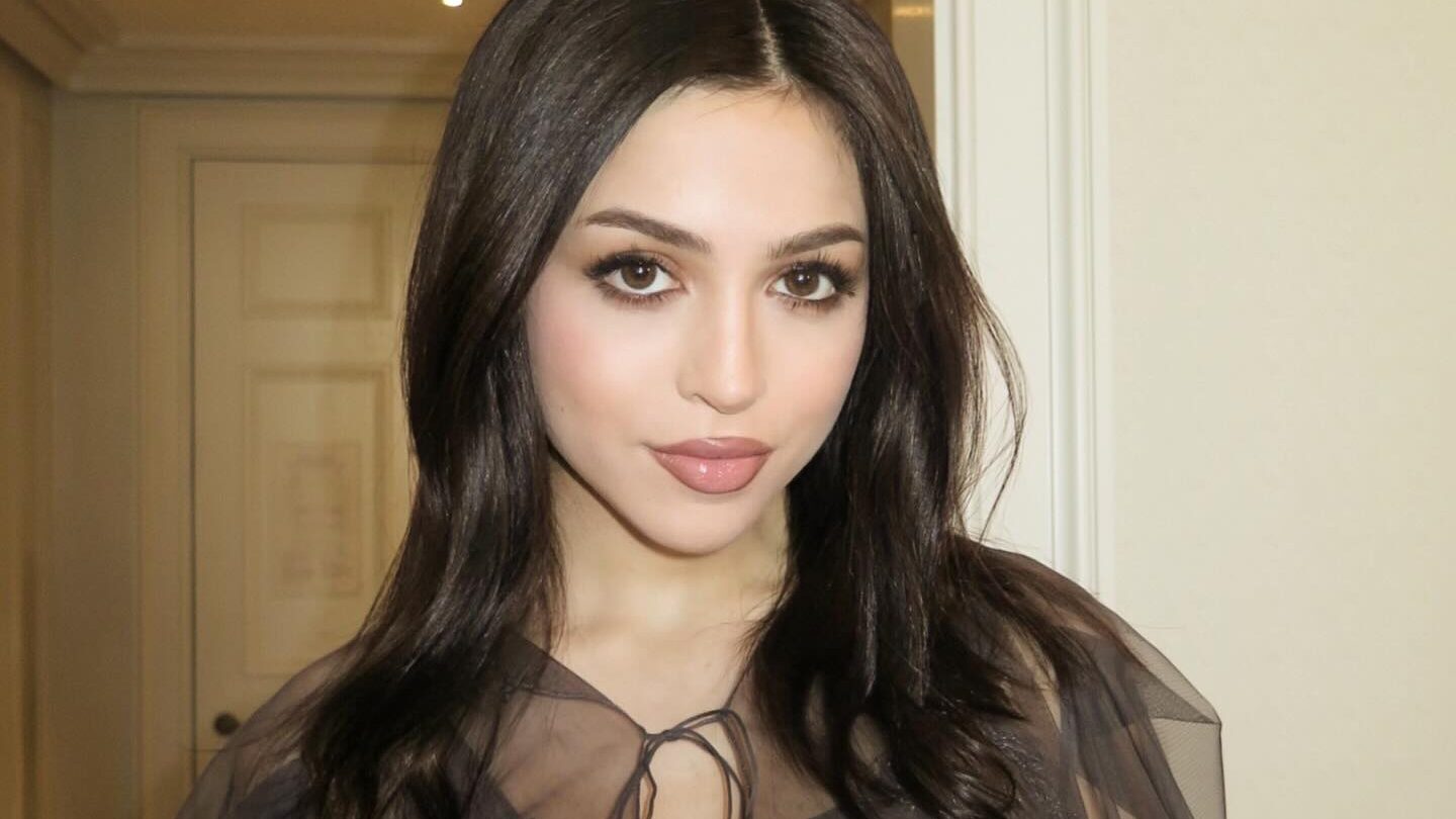 Josie Totah in London hotel hallway, dressed in black mesh top, makeup and hair styled for a glam look.