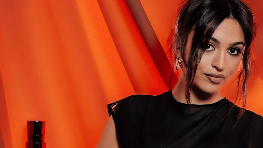 Josie Totah en robe noire ajourée à côté du parfum Divine, campagne Jean Paul Gaultier.