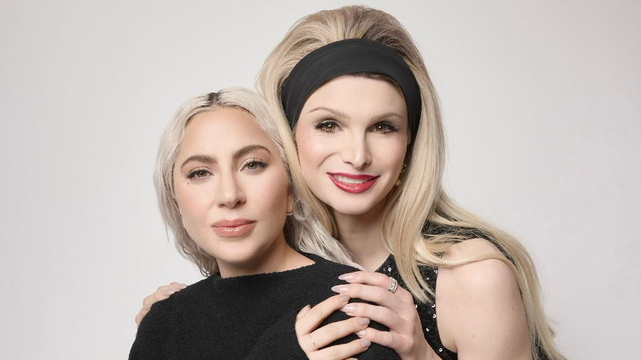 Dylan Mulvaney standing next to Lady Gaga, both smiling in a studio portrait.