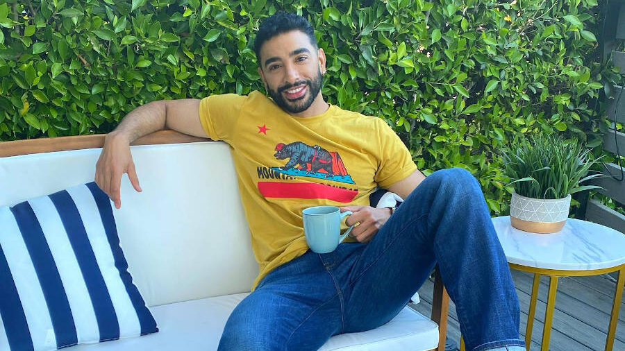 Laith Ashley assis sur un canapé d’extérieur blanc avec une tasse de café, souriant avec décontraction.