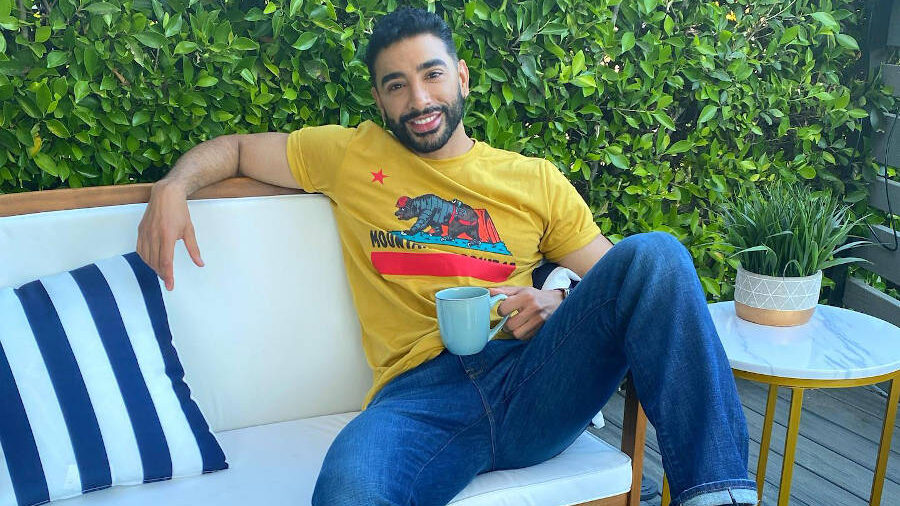 Laith Ashley seated on a white outdoor sofa with a coffee mug, smiling casually.