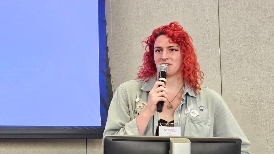 Lía Thomas debout à un pupitre avec un micro, s’exprimant lors d’une conférence trans en 2024.