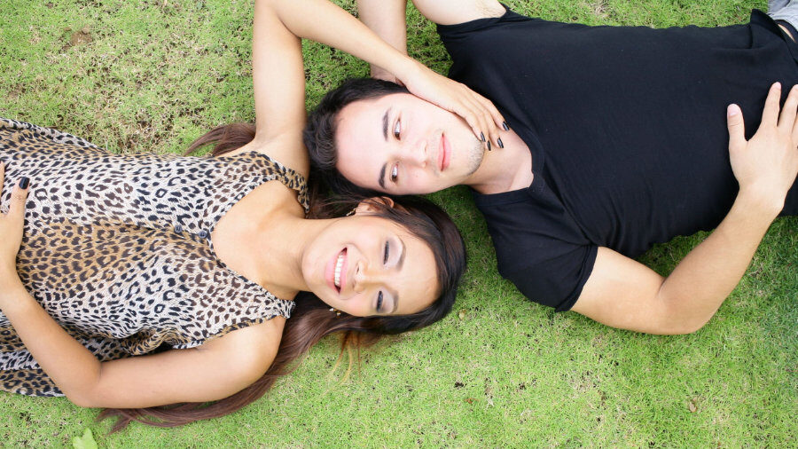 Mujer trans y su pareja acostados cara a cara al aire libre mientras disfrutan de un momento de paz.