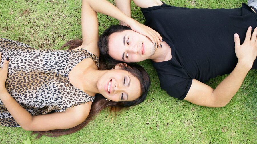 Trans woman and her partner lying face-to-face outdoors, enjoying a peaceful moment.
