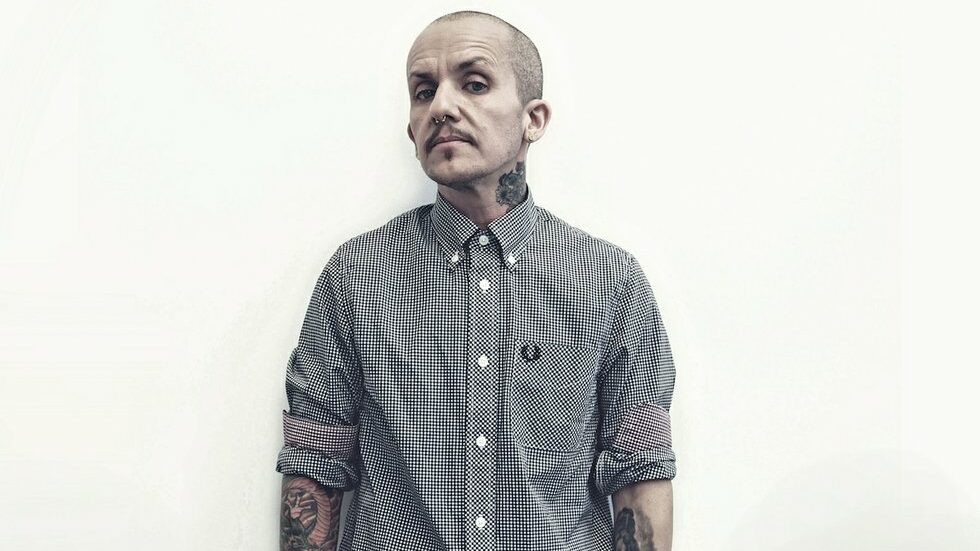 Lucas Silveira stands against a white wall in a Fred Perry shirt for Anchor Campaign.