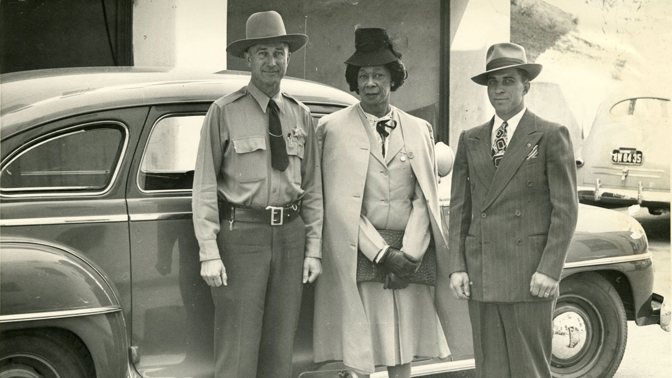 Lucy Hicks Anderson entre les adjoints du shérif H.E. Bowman et Charles Salig, devant une voiture ancienne, vers 1945, dans le comté de Ventura, en Californie.