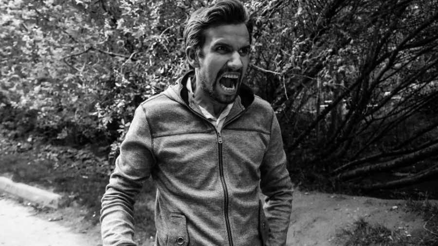 Image en noir et blanc d'un homme en train de crier, entouré d'arbres et de buissons.