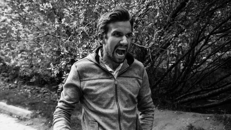 Black-and-white image of a man shouting, surrounded by trees and bushes.