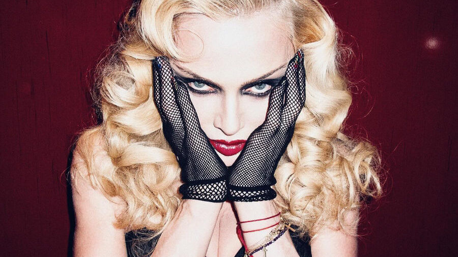 Madonna in black outfit and mesh gloves, posing with intense gaze.