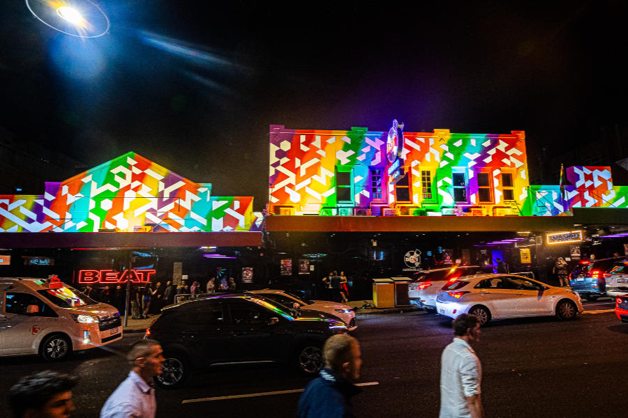 Exterior of The Beat Megaclub in Brisbane with rainbow lights and people walking by.