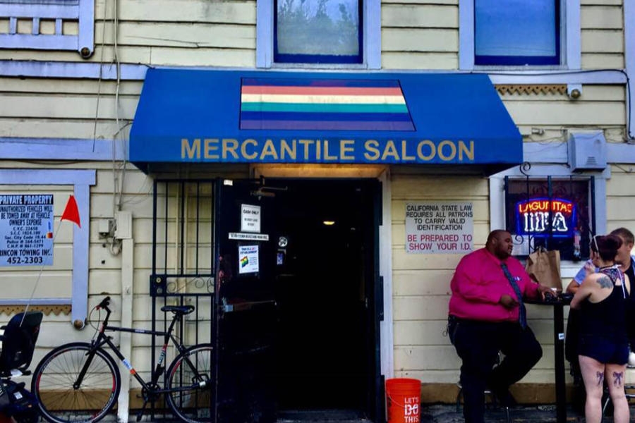 Entrance of Mercantile Saloon, Sacramento’s historic gay bar, with pride flag awning and people chatting outside.