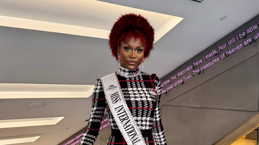 Midori Monet, in a plaid dress with red fur cuffs and sash, poses at NYC’s Gender Affirming Care Conference venue.