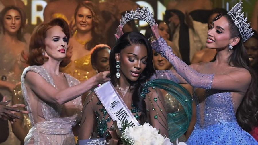 On stage, Midori Monet receives her crown as Miss International Queen USA 2025, wearing an emerald green gown and holding white orchids.