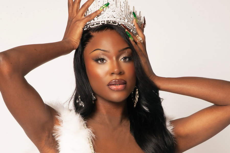 Midori Monet poses in a white feather-trimmed outfit with crown and earrings, celebrating her win and Black History Month.