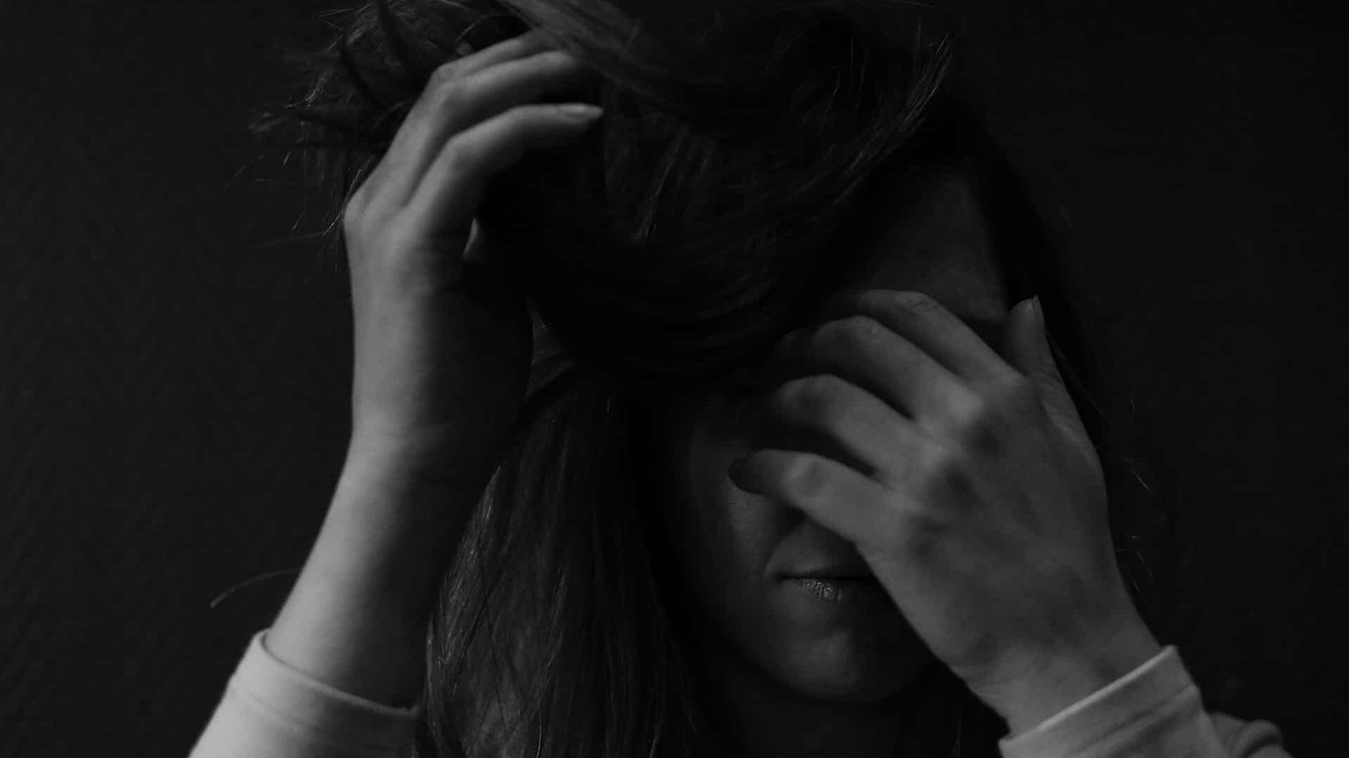 Black and white close-up of a person covering their face with their hands, conveying distress or emotional overwhelm.