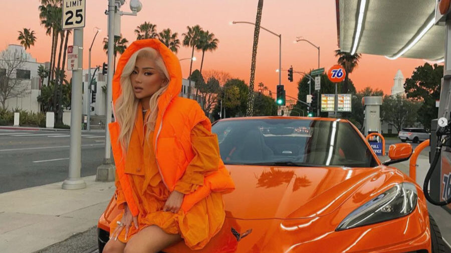 Nikita Dragun con un conjunto naranja brillante, sentada sobre el capó de un Corvette del mismo color en Los Ángeles.