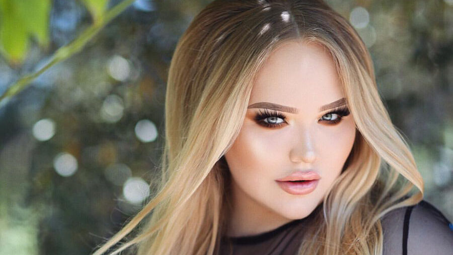 NikkieTutorials with long blonde hair in black mesh top embroidered with flowers.