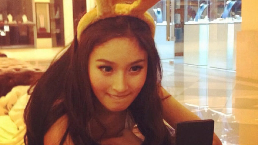 Gros plan de Nong Poy regardant son téléphone, portant des oreilles de lapin, dans une boutique éclairée chaleureusement.