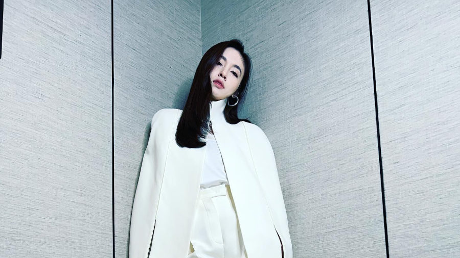 Treechada Petcharat standing elegantly in a white suit at a 2022 Bangkok press conference.