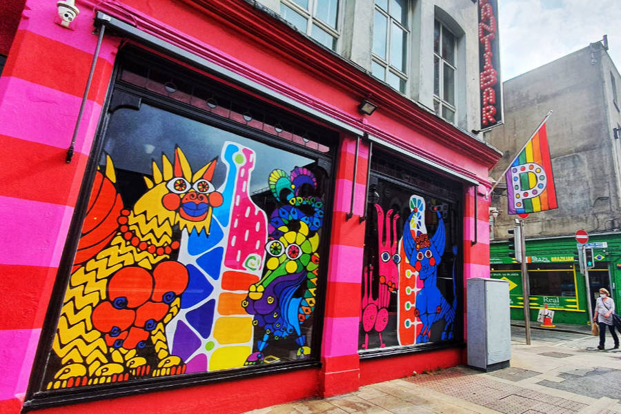 Front of Pantibar in Dublin with colorful mural art on the windows and a rainbow flag.