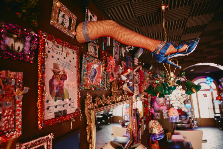 Interior de un bar temático de drag con una lámpara de pierna de maniquí y fotos enmarcadas con brillos.