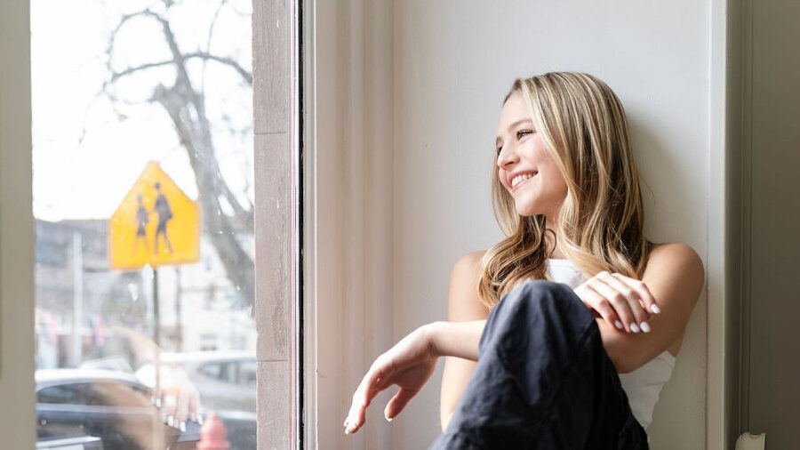 Rebekah Bruesehoff in casual clothes seated indoors near bright window.