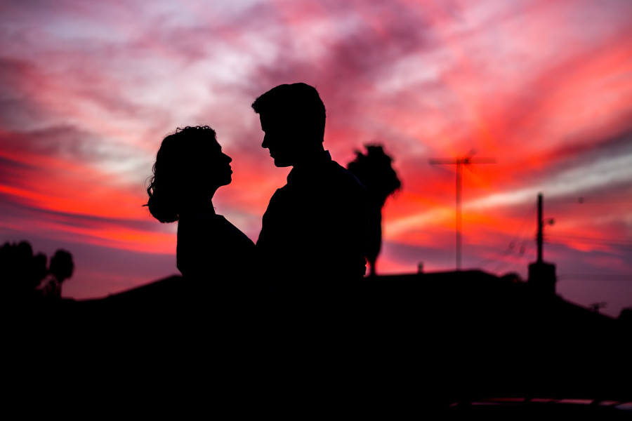 Silhouettes of a couple facing each other at sunset, with vivid pink and orange clouds in a Parisian sky.