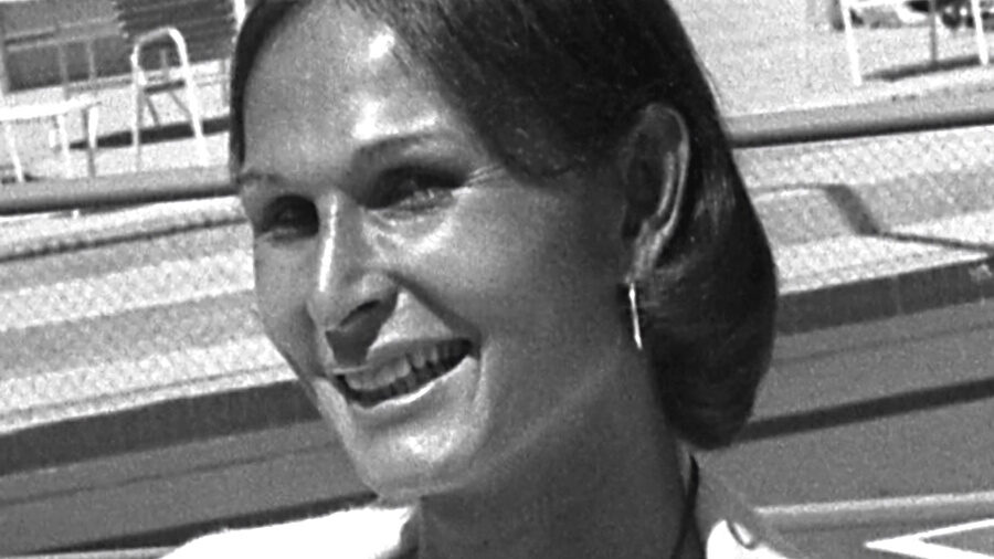 Renée Richards souriant lors d’une conférence de presse en 1976 dans un club de tennis à Newport Beach, portant des boucles d’oreilles et un chemisier.