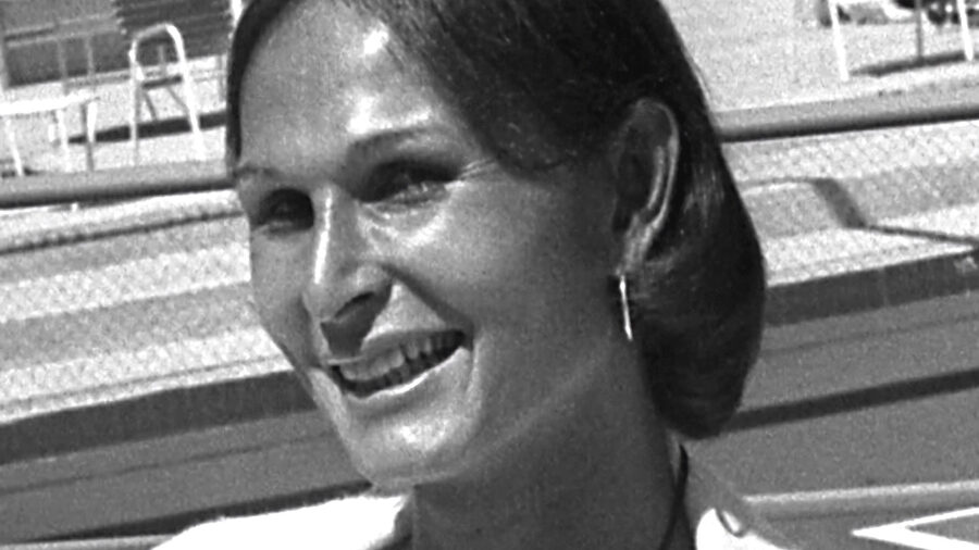 Renée Richards sonriendo durante una rueda de prensa en 1976 en un club de tenis de Newport Beach, con pendientes y blusa.